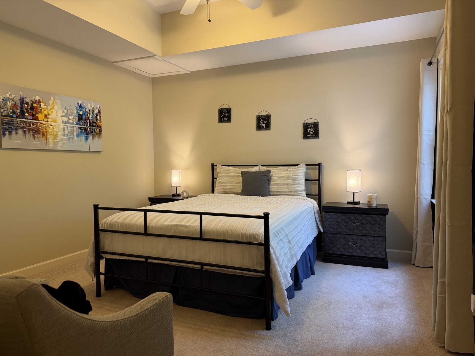 Bedroom with a queen bed in a black metal frame, matching nightstands with lamps, and colorful artwork at Butterfly Lake Retreat
