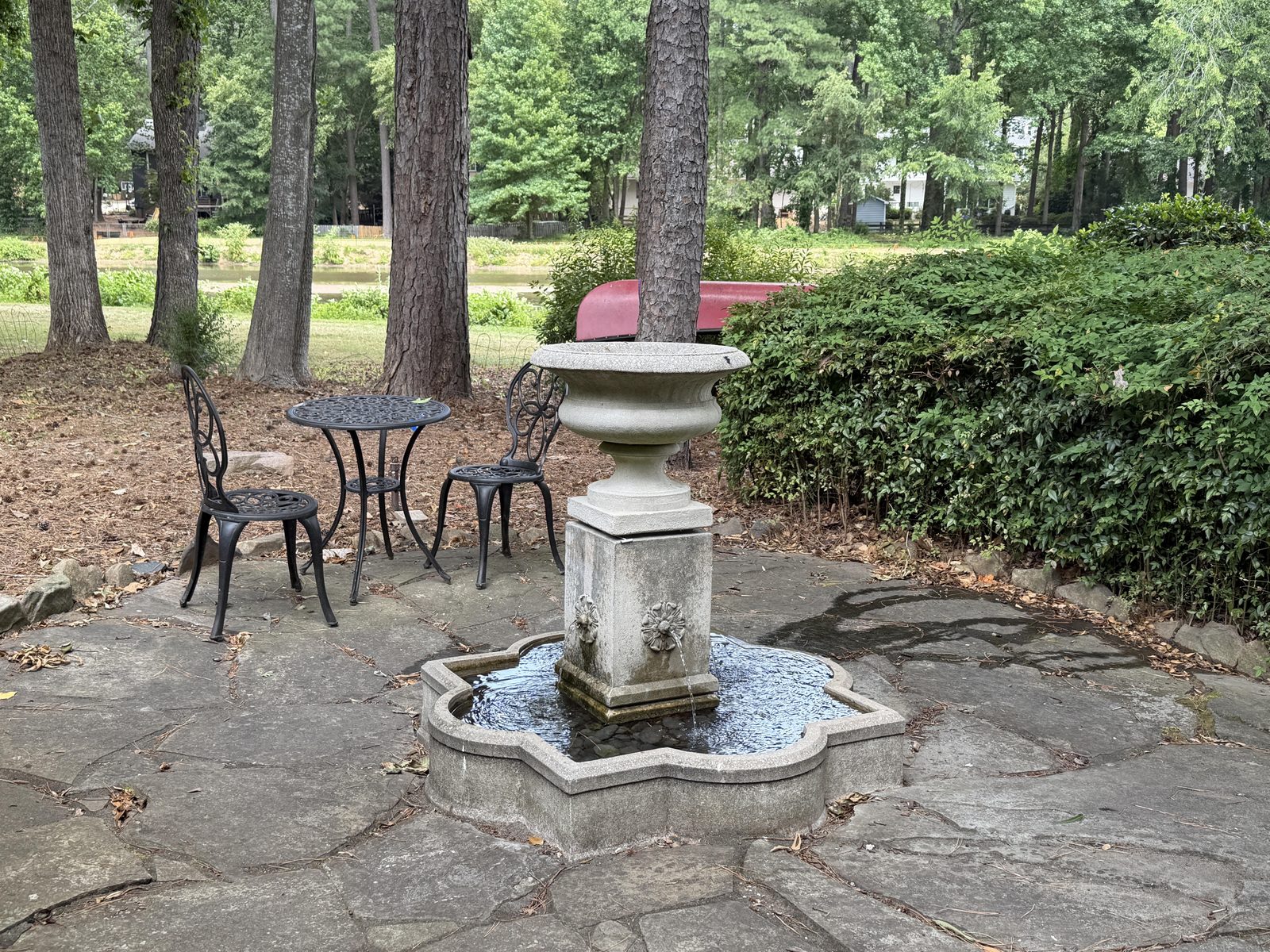 Stone garden fountain with a bistro table and chairs on a flagstone patio under tall pines, the canoe and lake beyond at Butterfly Lake Retreat