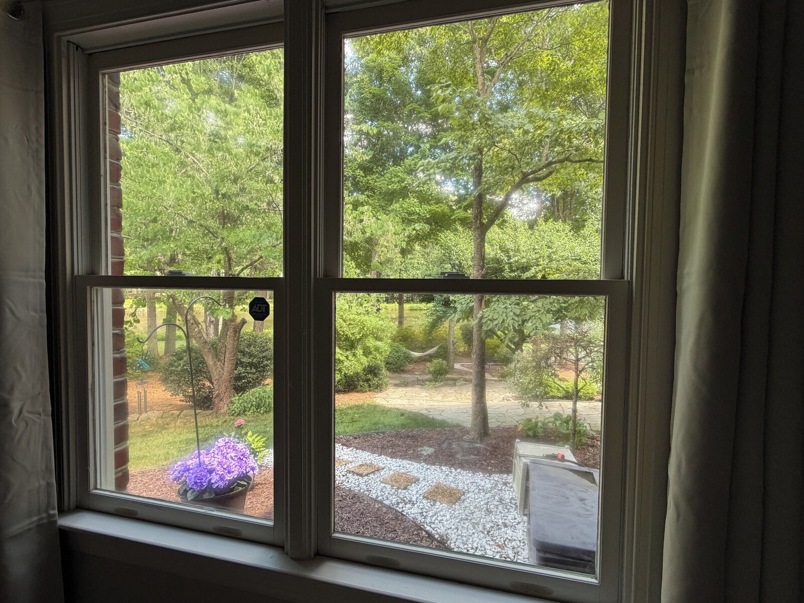 Window view of the pollinator garden with trees and a gravel path at the lakefront suite