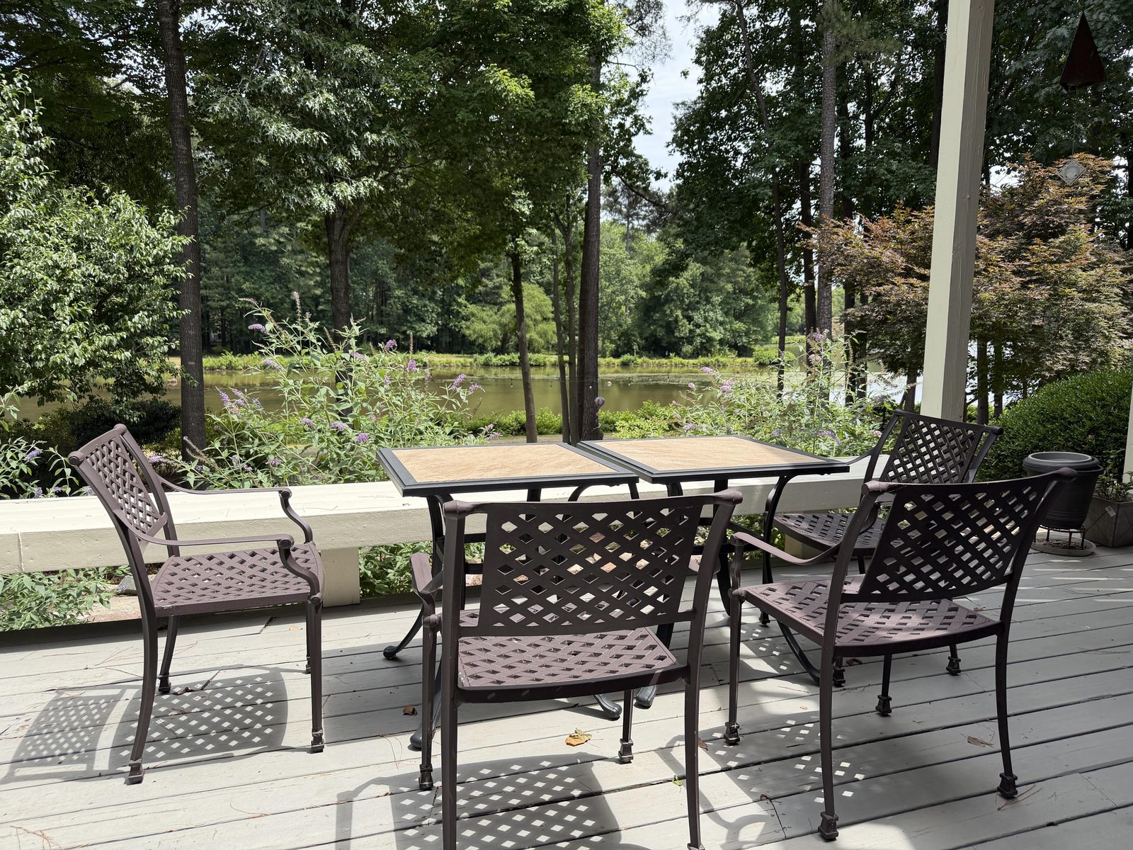 Lakeside deck with a patio dining set of metal lattice chairs and tables overlooking the lake through the trees at Butterfly Lake Retreat